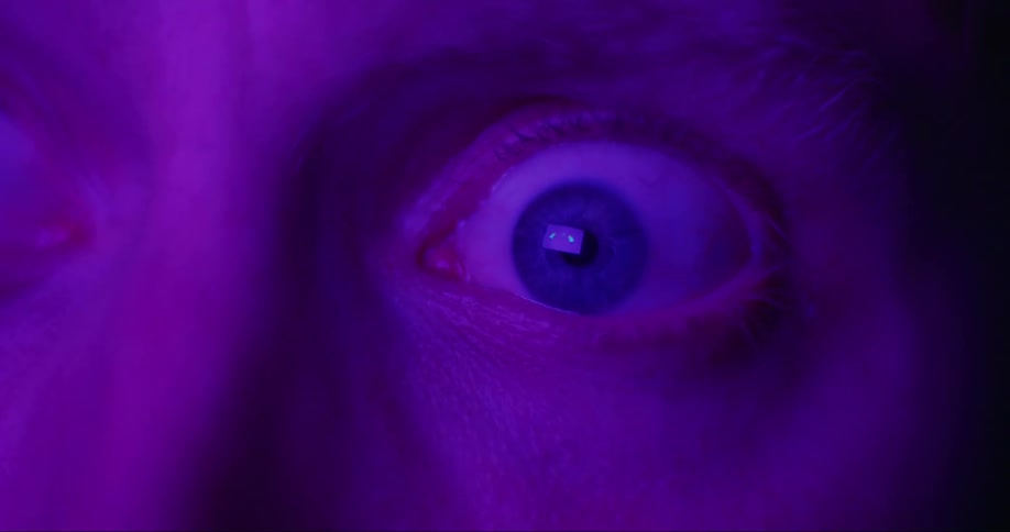 An extreme close up of a persons eyeball wide open as if in fear as different light flares strobe across his face