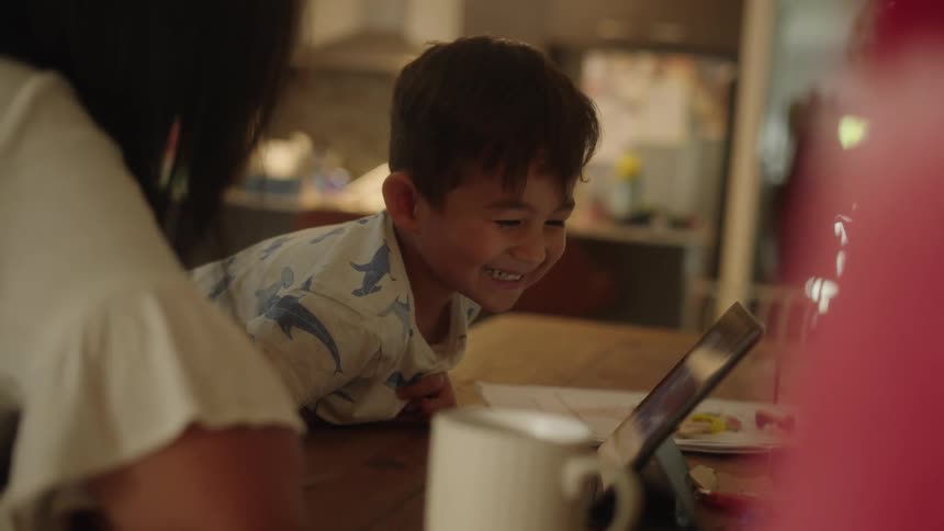 A boy watching a tablet smiling and laughing and looking at the woman next to him