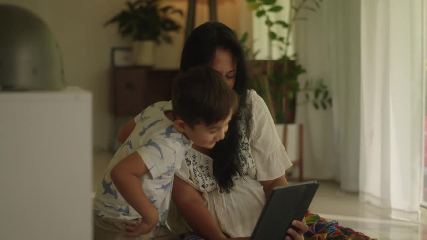 A boy kisses his mother on the cheek while they look at a tablet and smile
