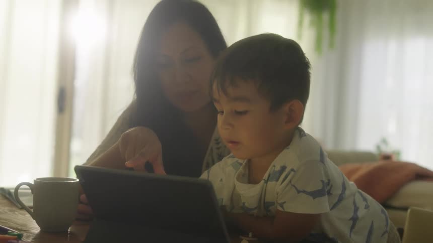 A boy and his mother look at a tablet screen together as the mother smiles and laughs
