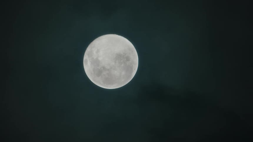 Nighttime sky with clear view of full moon but with clouds or fog moving past