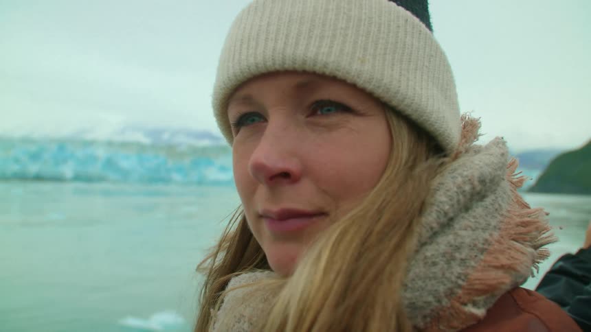 Woman and another person on a boat in the middle of an icy lake with blue glacier ice in the background