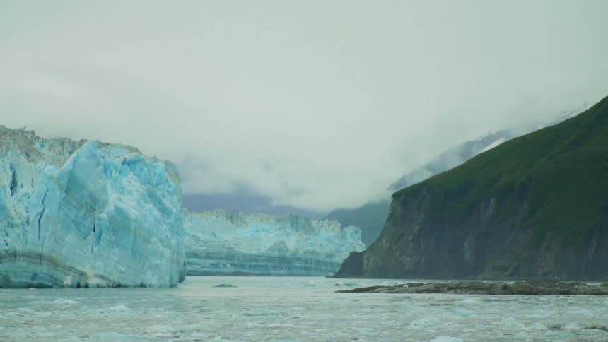 Sea ice fills ocean between glacier and cliffs under an overcast sky