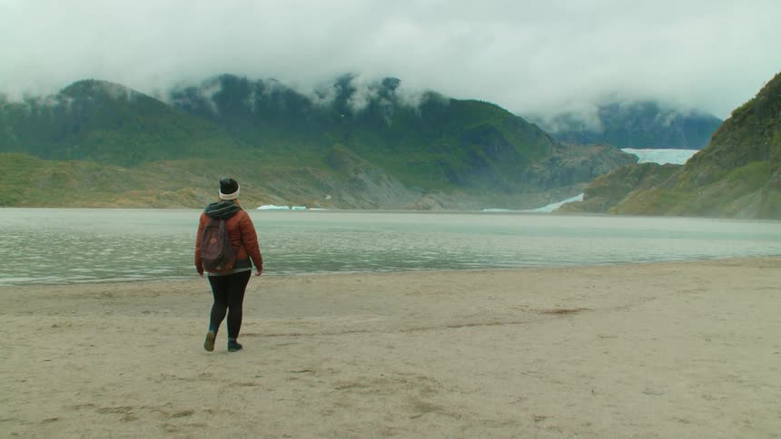 A woman hiking on a beach walks toward the water