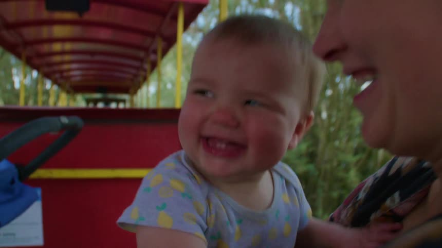 Mother and baby laughing and smiling together while on train ride in the park or zoo