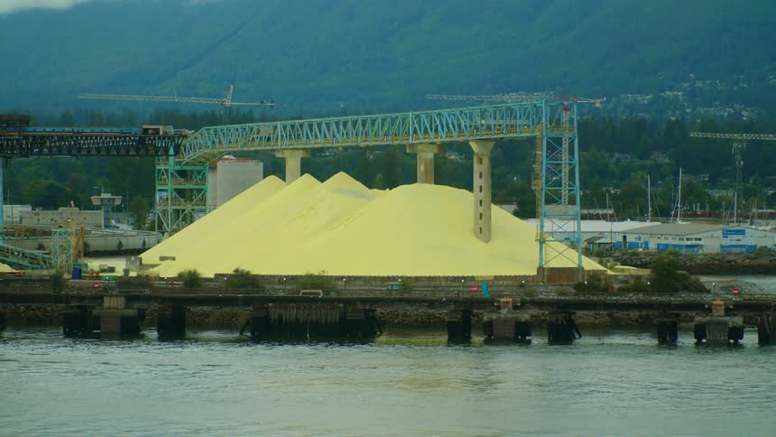Large yellow mound sits near waterfront with marina and mountains in the background