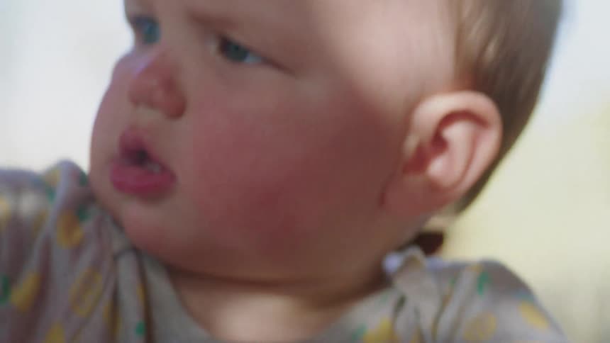 Light shines on a babys face as they reach out and look to the side trying to talk
