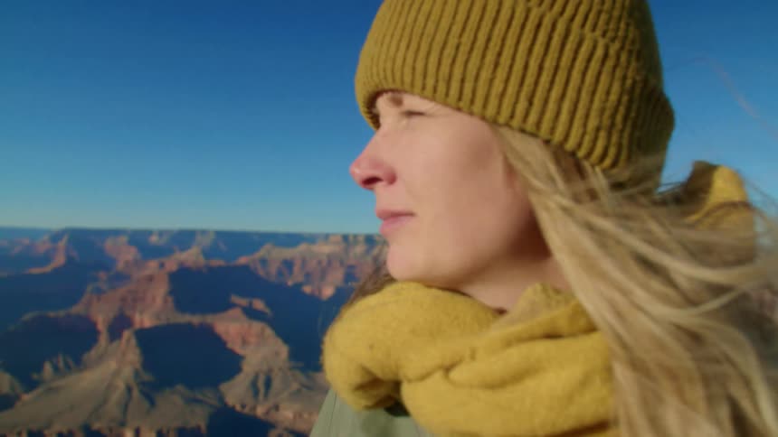 A blonde woman stands at a vista point and looks at the grand canyon