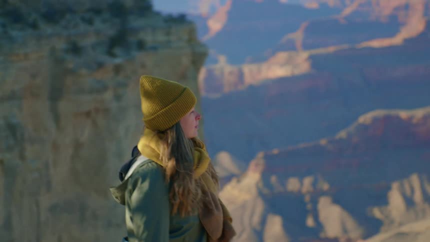 Woman wearing knit hat and coat walks along edge overlooking canyon