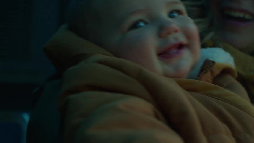 Blonde mother with wooly hat holds son in yellow coat laughing