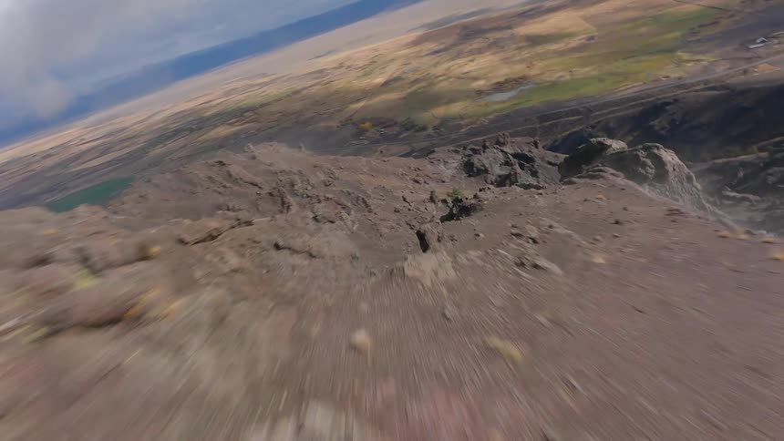 A high speed FPV drone shot rushing through rough and rugged mountain towers over plains that stretch to foggy mountains on the horizon