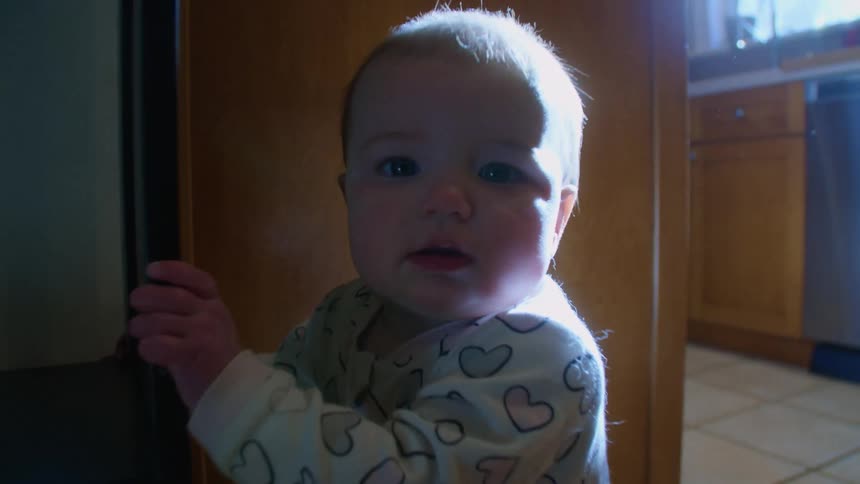 Baby in baby bodysuit stands in the kitchen