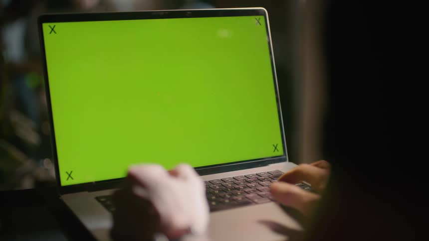 Person working on laptop at night laptop has replaceable green screen with tracking points