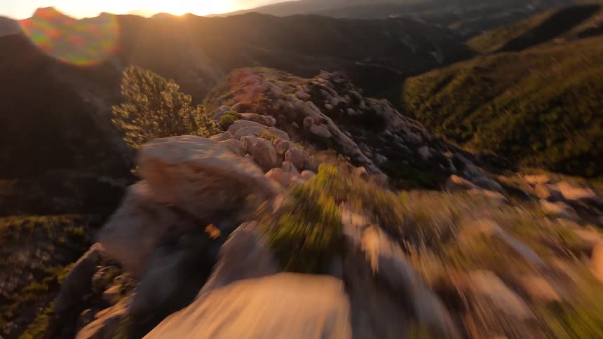 High speed FPV drone view going down a rocky mountain with the sunlight flaring in the sky