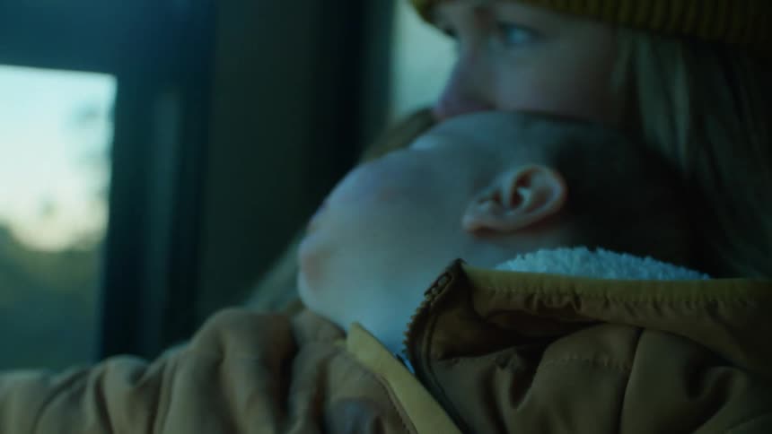 A woman sitting in the passenger seat of an automobile holds and kisses her baby as they travel on the road