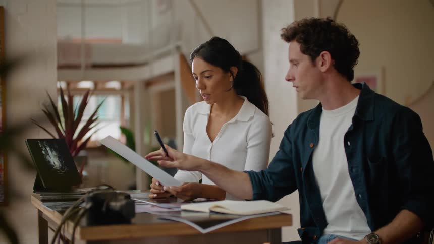 Man and woman in creative office environment sitting at a table and discussing designs plans details