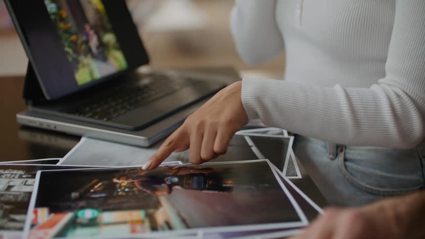 Young woman standing next to a laptop looking at printed pictures