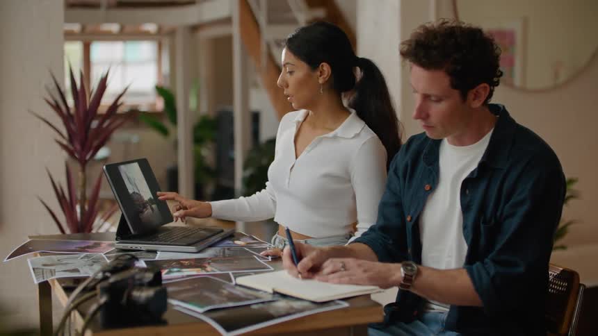 Man in dark blue shirt and woman with ponytail and white shirt use tablet and write down in notebook