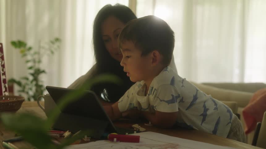 Mother and son uses tablet at table in the living room