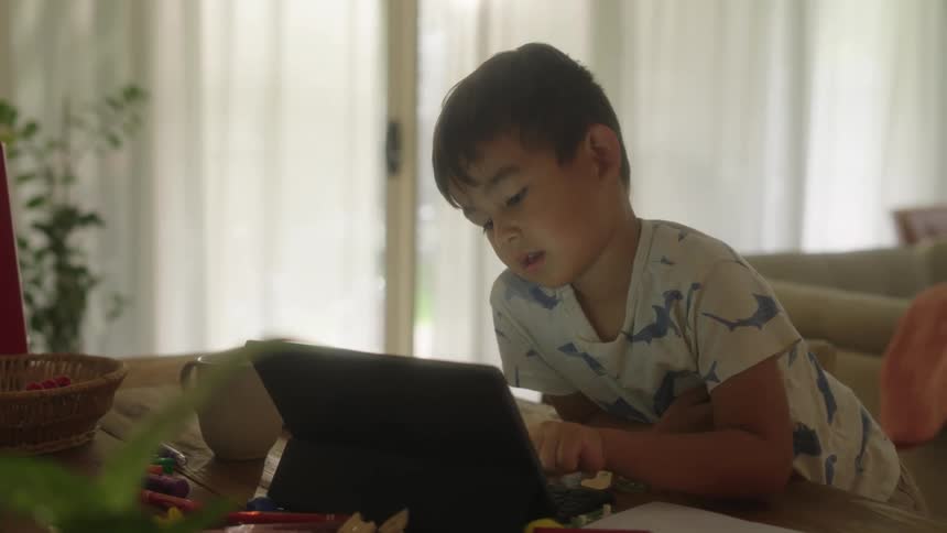 Young boy sitting at dining table working on laptop probably home school