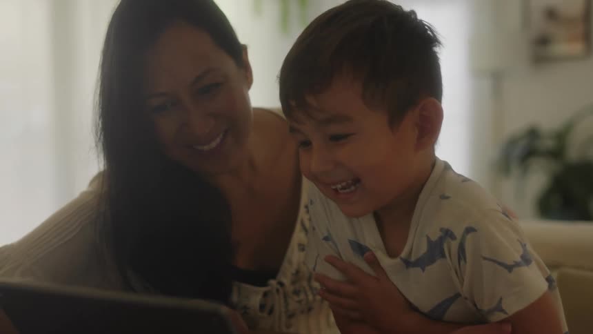 A boy and his mom laugh while watching something on their laptop