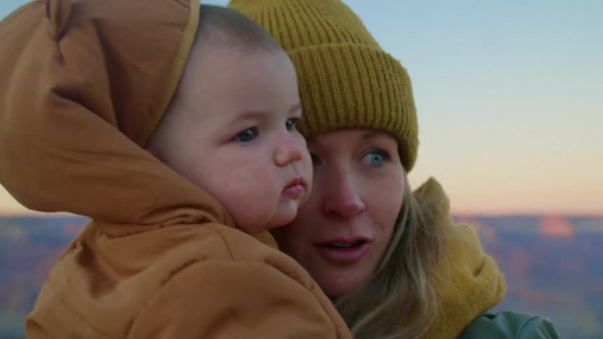 A mother holding her baby outdoors with mountains in the background