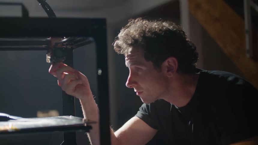 Man works on 3d printer setup near staircase