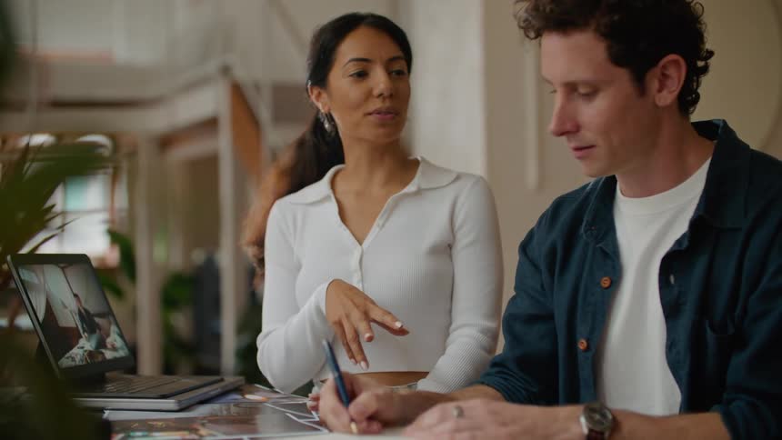 A man and woman standing next to each other in front of a laptop working talking and writing