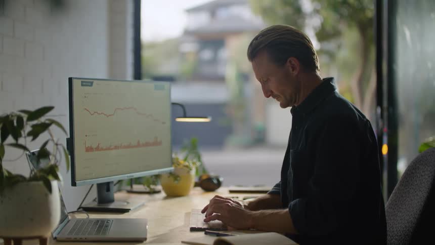 Man in black shirt sits at desk typing on computer keyboard in the office