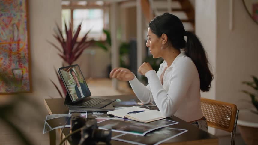 Woman sitting at table shows one of several pictures to man she is video calling with