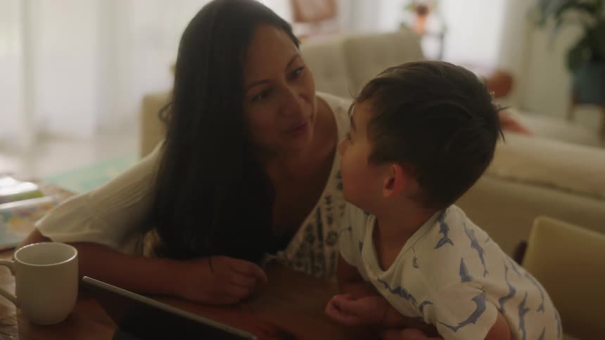Mother and son watch tablet sitting at table in the living room at home