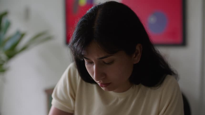A woman sitting at a desk writing on papers while looking up ahead of her