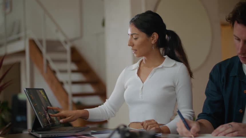Man in white top and dark blue shirt looks at tablet and writes down talking with woman with ponytail and white shirt at desk in building