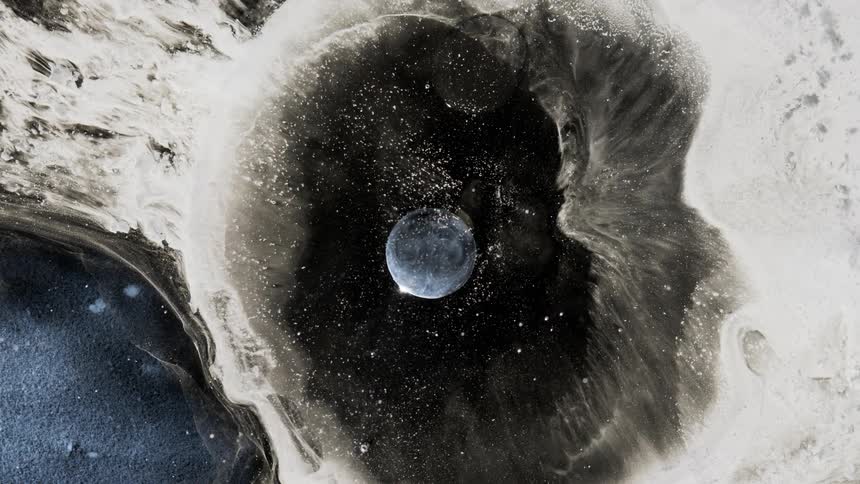 Streaky pale mass flows into black center with blue sphere and bubbles