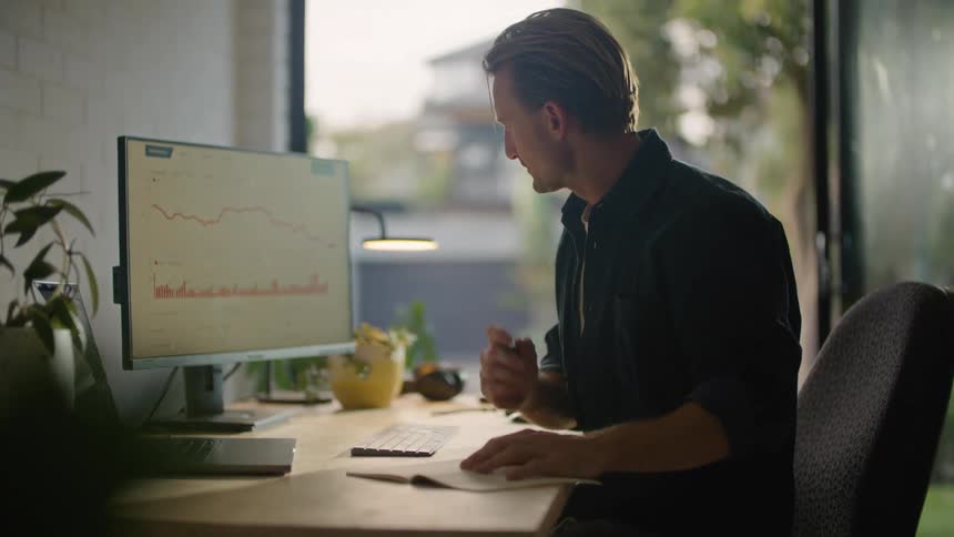 Businessman in black shirt writes down in notebook looking at computer screen at the office