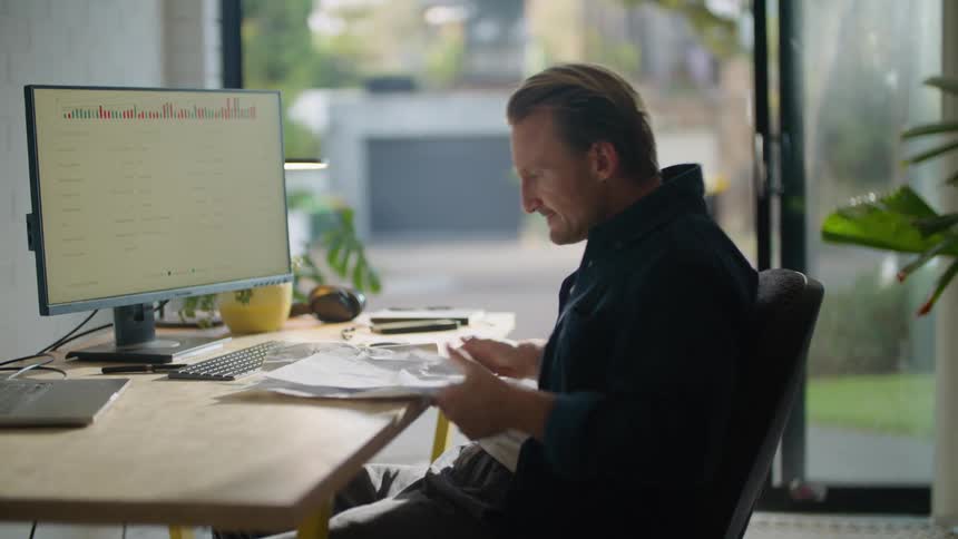 A man sitting at his desk looking through papers then throwing them up in the air in frustration and putting his head down on the desk