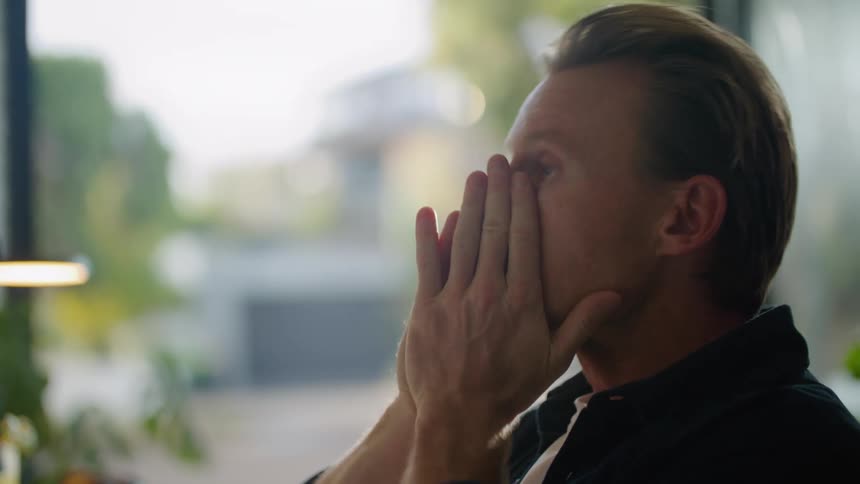 A mans face as he looks at pieces of paper and then puts his hands on his forehead in frustration