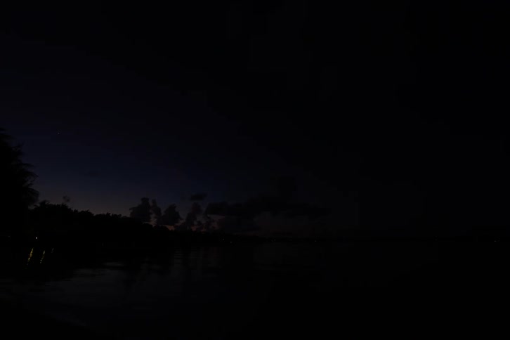 Clouds roll over a seaside village and lights come on as the sun sets