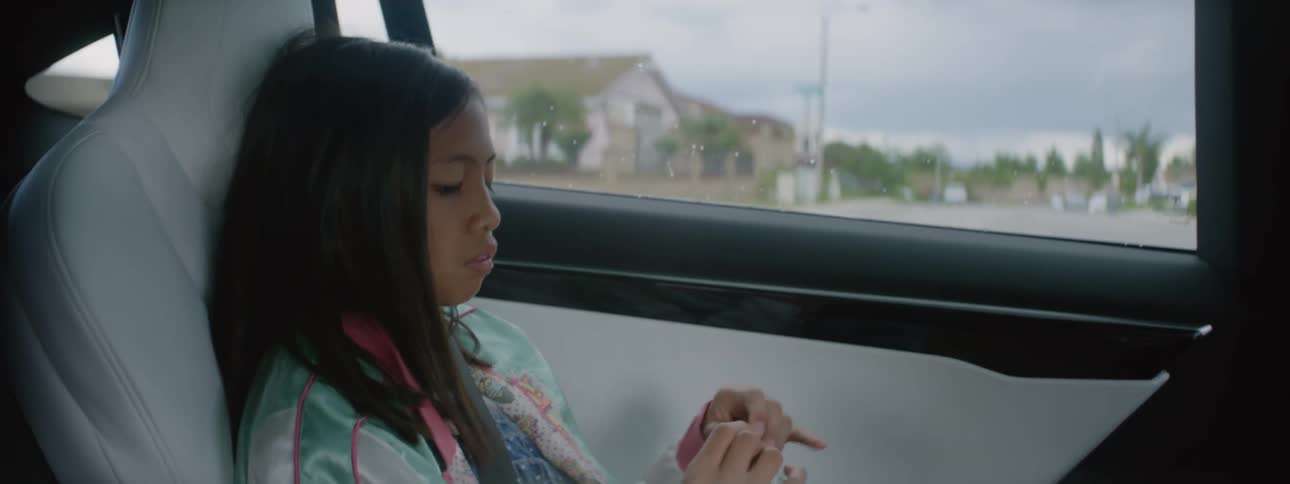 A girl sits in a passenger seat of a vehicle playing with something in her hands