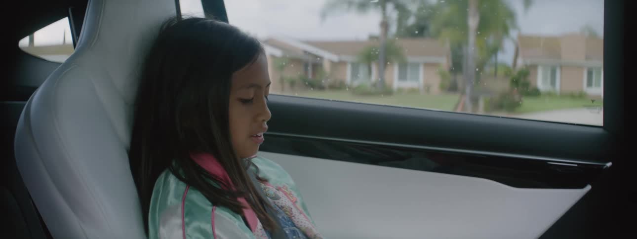 The view is of a kid that is sitting in a car while someone is driving
