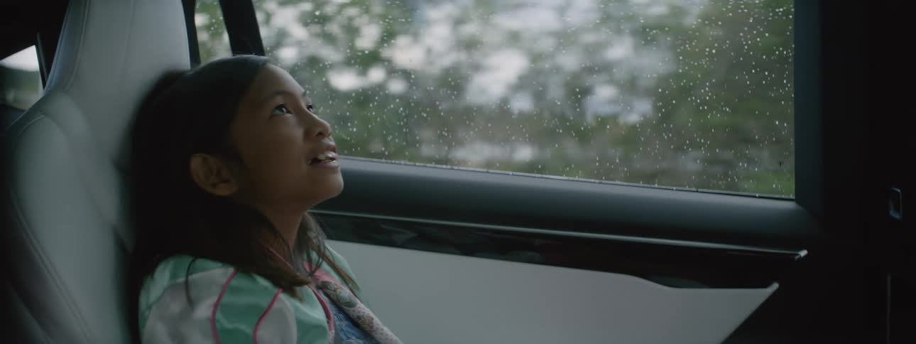 A young girl sitting and riding in a car as trees and plants go by