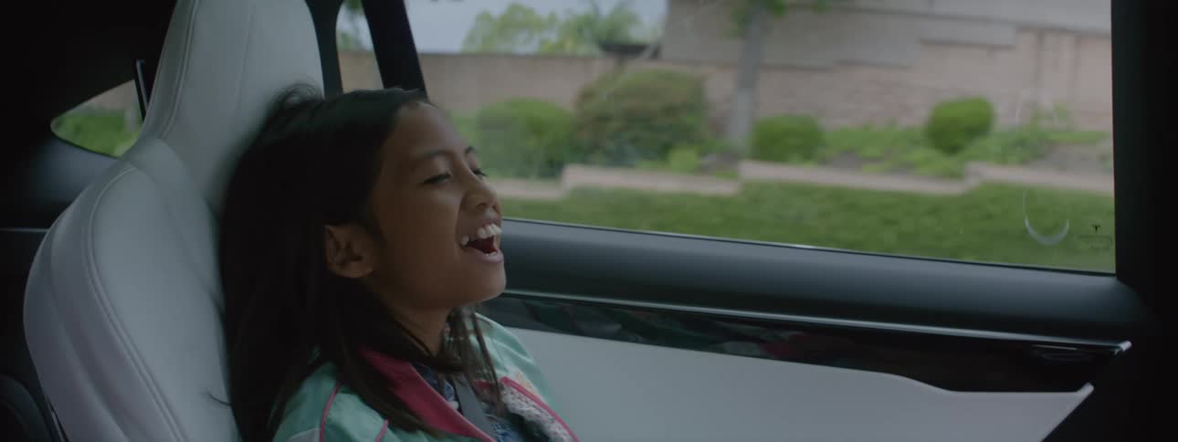 A young girl riding in the back of a car laughing and smiling and talking