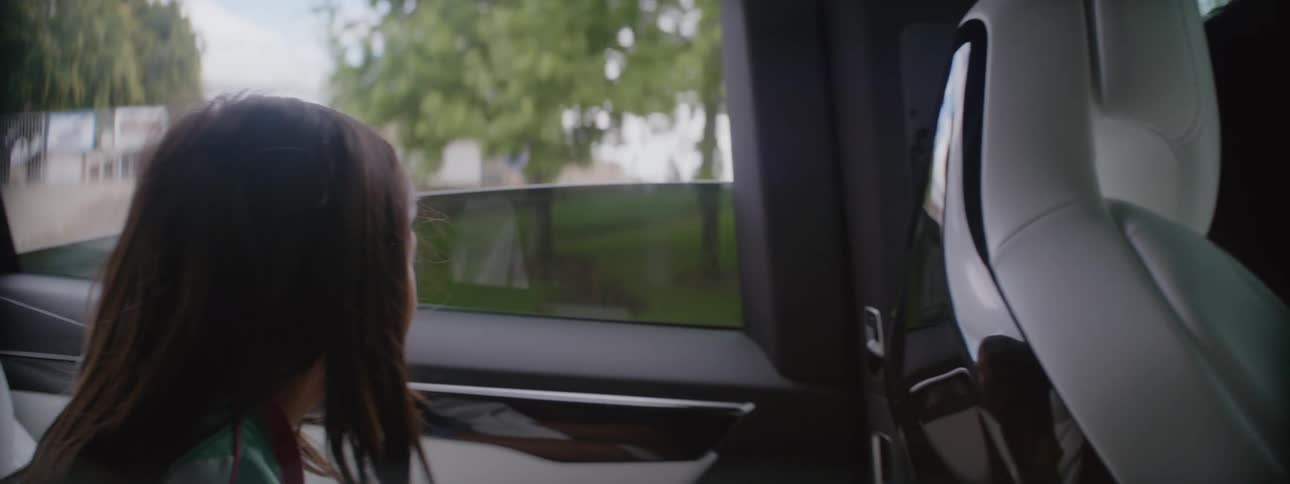 A woman is driving an automobile and her little girl is sitting in the back seat looking around