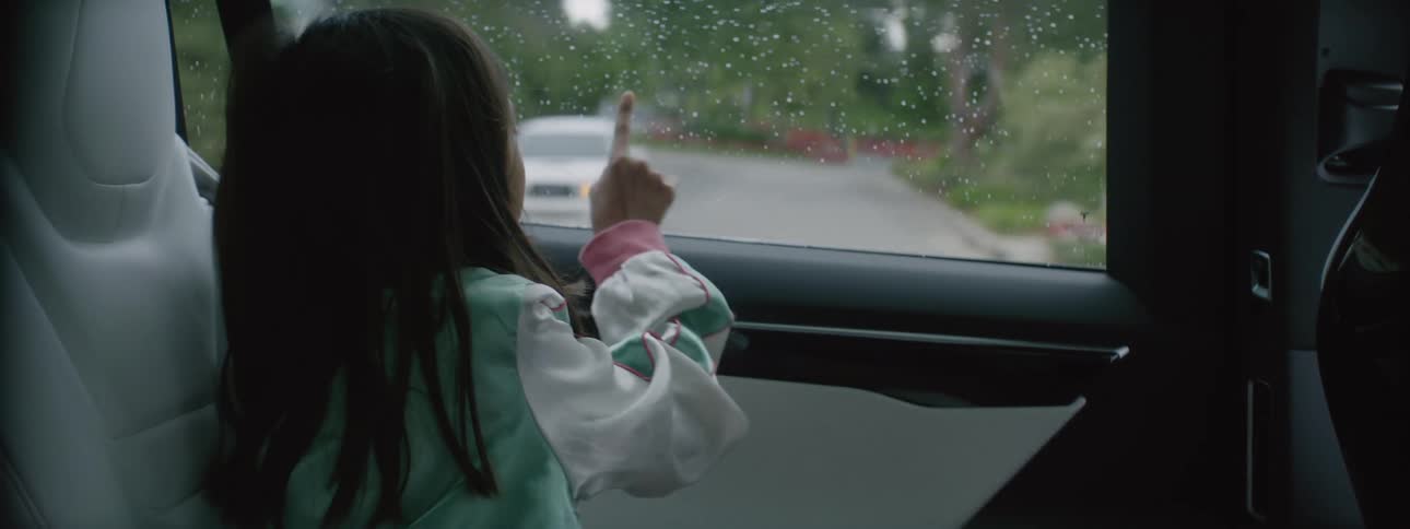 A girl playing with a car window while the car drives