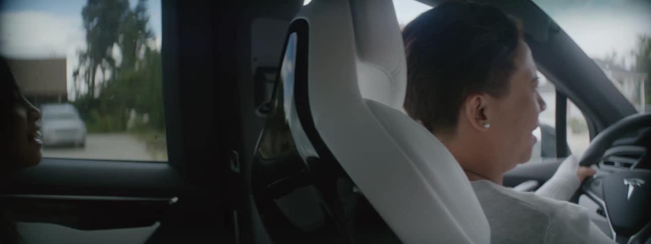 A woman is driving an automobile through a neighborhood and her little girl is sitting in the back seat
