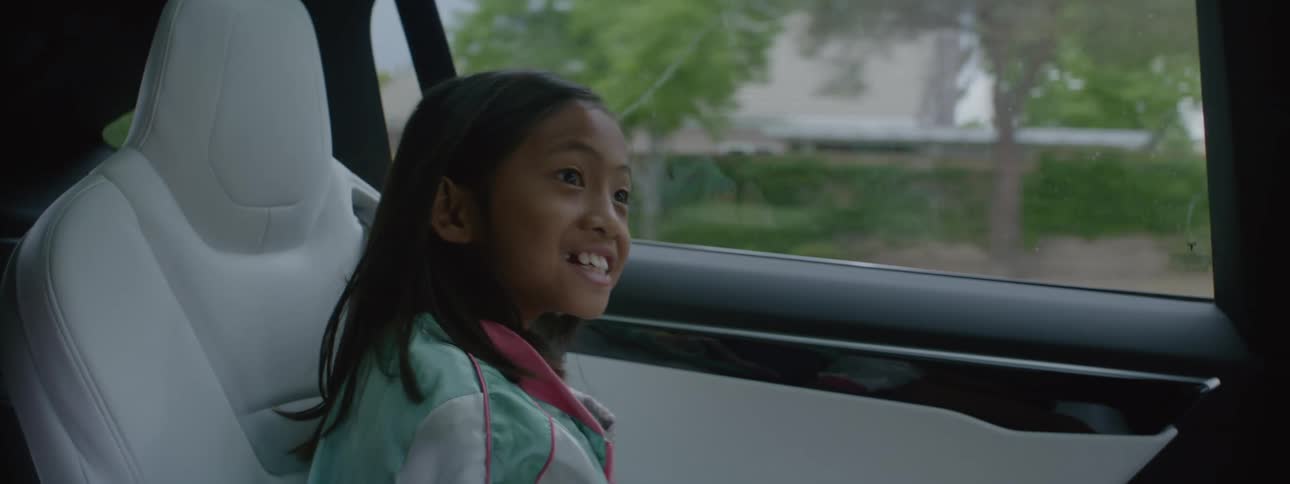 A young girl sitting in the back of a car smiling laughing and talking to someone in front