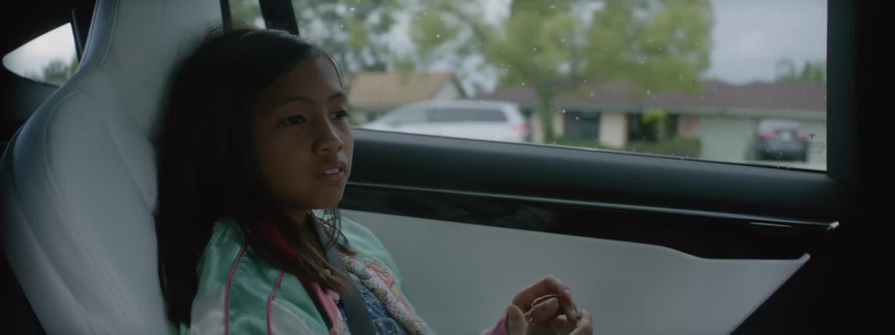 Girl looks around while sitting on the back seat of a car driving through town