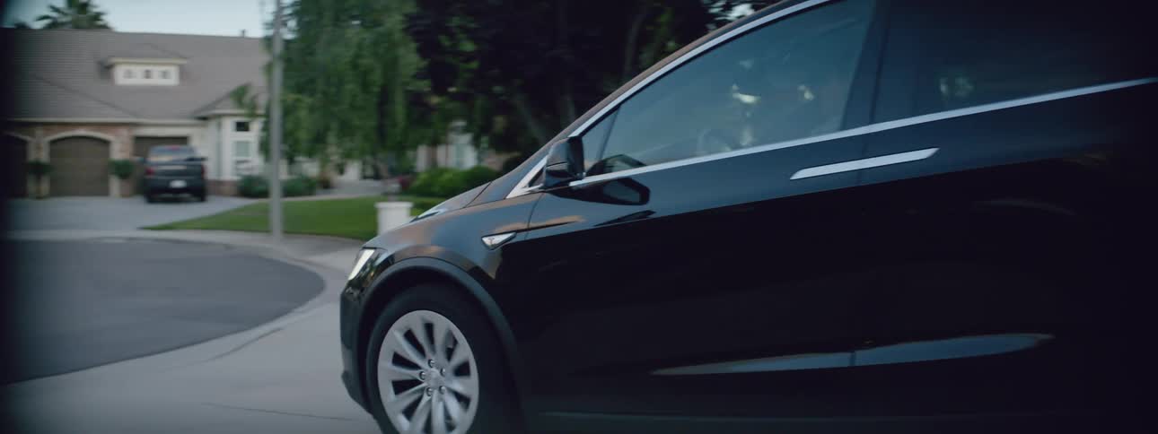 A black luxury sedan drives out of the garage in the suburbs at morning
