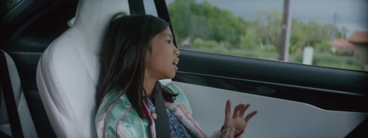 A girls is sitting in the seat of an automobile and playing with a bracelet as she looks out the window