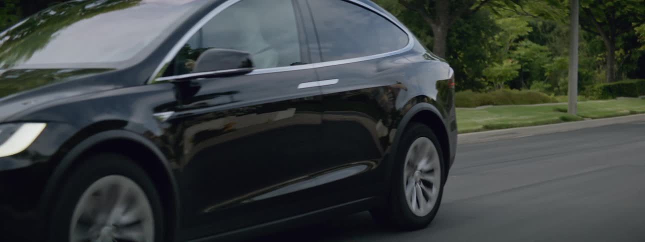 A black automobile is traveling on a neighborhood street